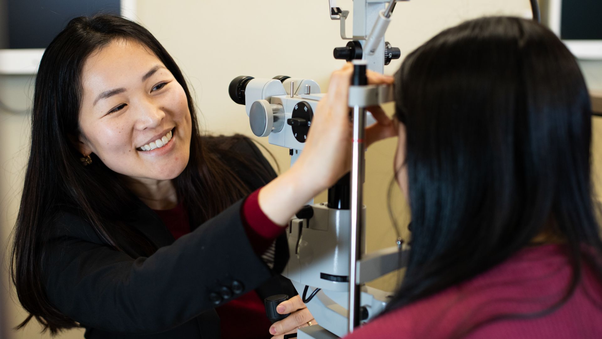 Woman using equipment to examine someone's eyes, smiling